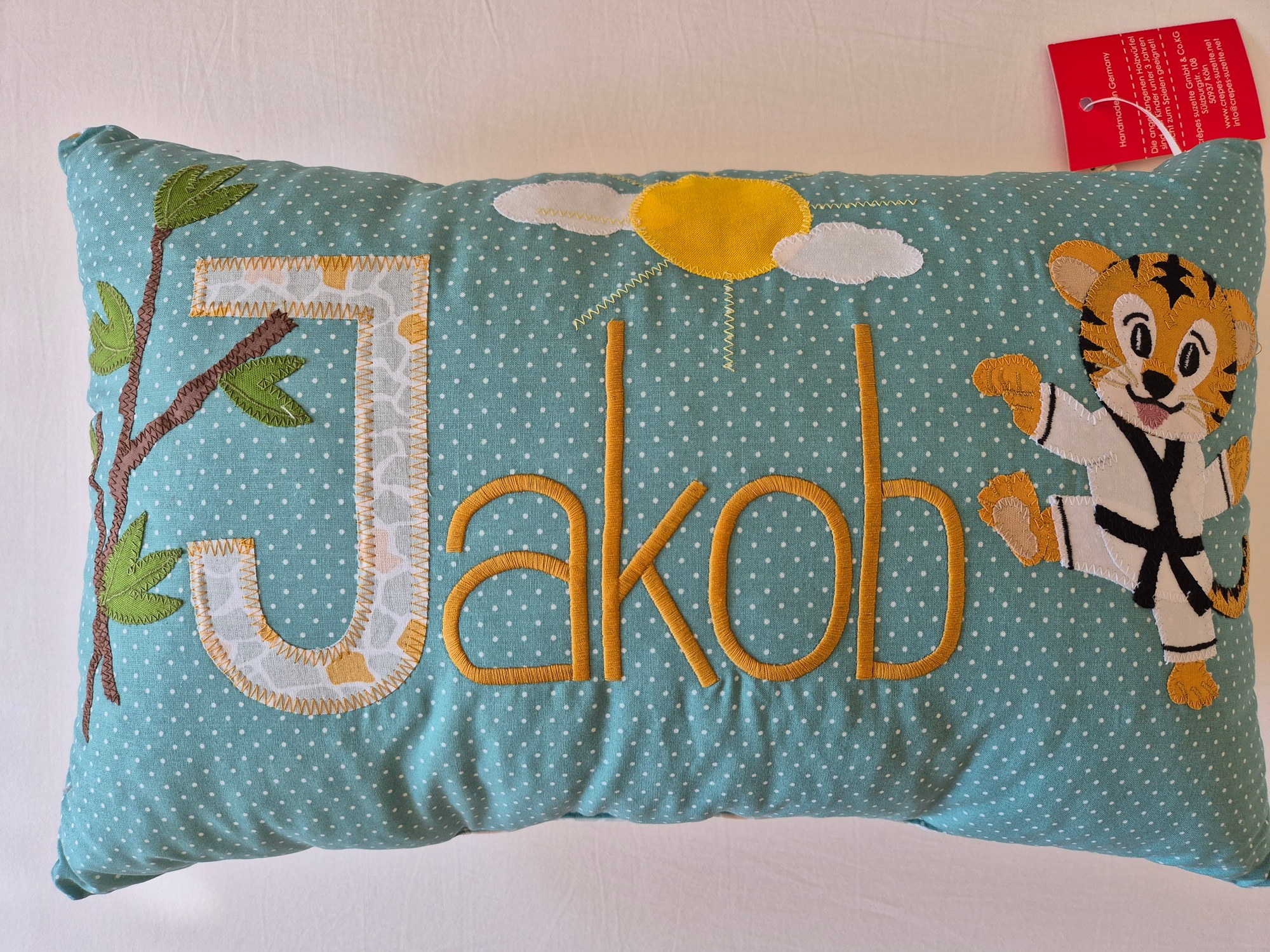 Unsere Karate-Baby-Tradition: Jakob hat sein Kissen 1 Türkisfarbenes Namenskissen mit dem Namen Jakob in goldener Schrift, daneben ein Tiger im weißen Karateanzug mit schwarzem Gürtel, darüber Sonne und Wolken